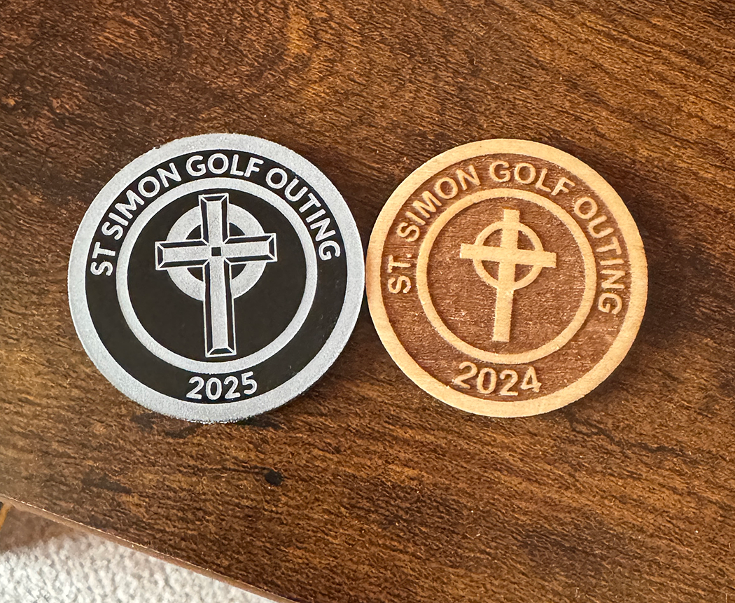 Two round stickers with 'St. Simon Golf Outing' logos on a wooden surface.